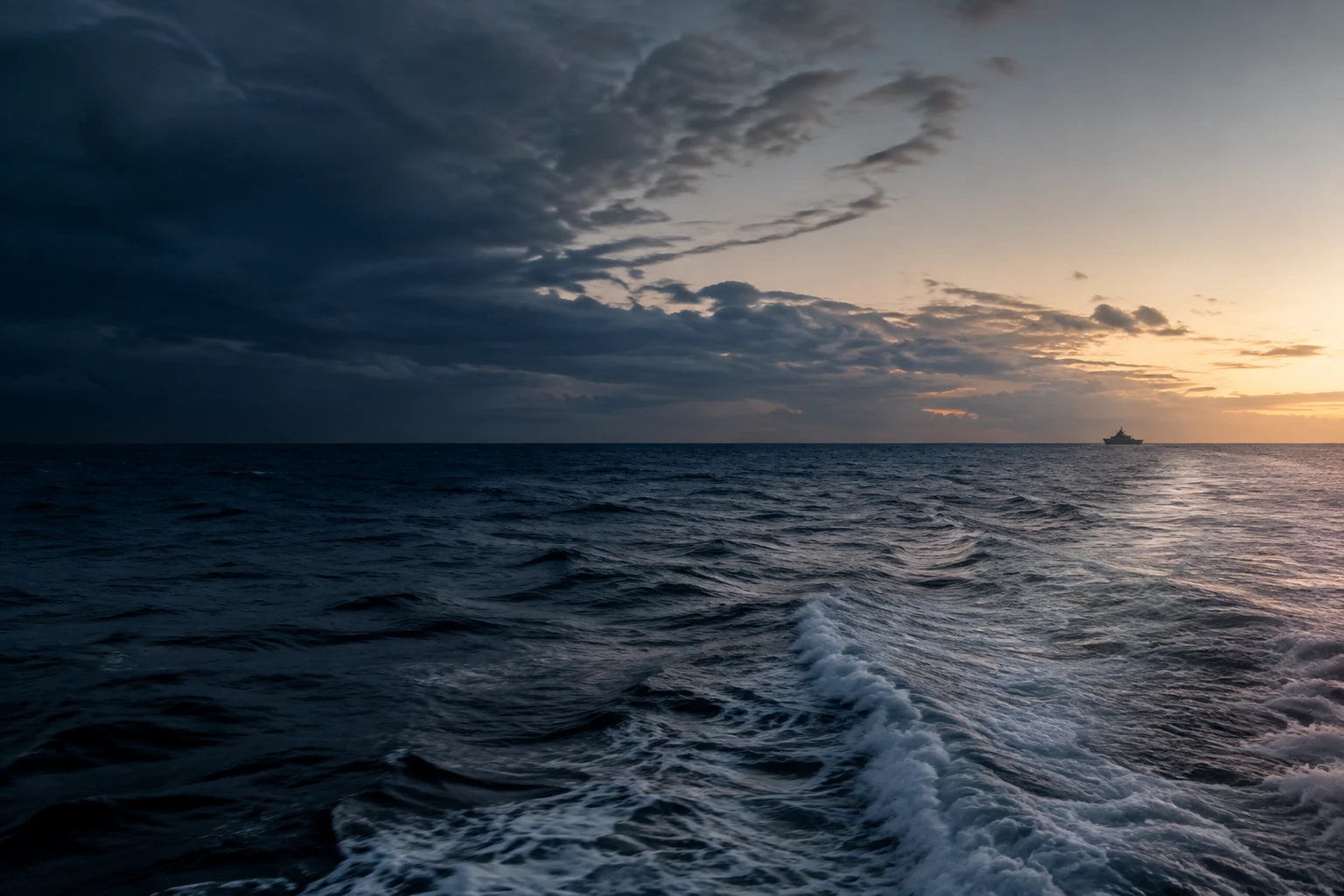 White wake across a deep blue sea, with a distant ship on the horizon